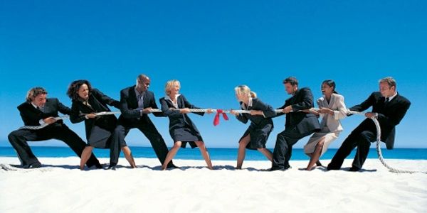 Business team playing tug of war on the beach.