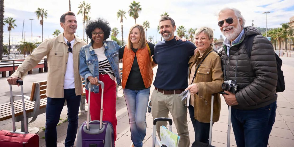 Group of six friends with luggage smiling outdoors.
