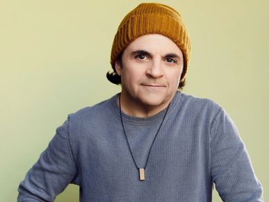 Man wearing a mustard beanie and gray sweater with a pendant necklace.