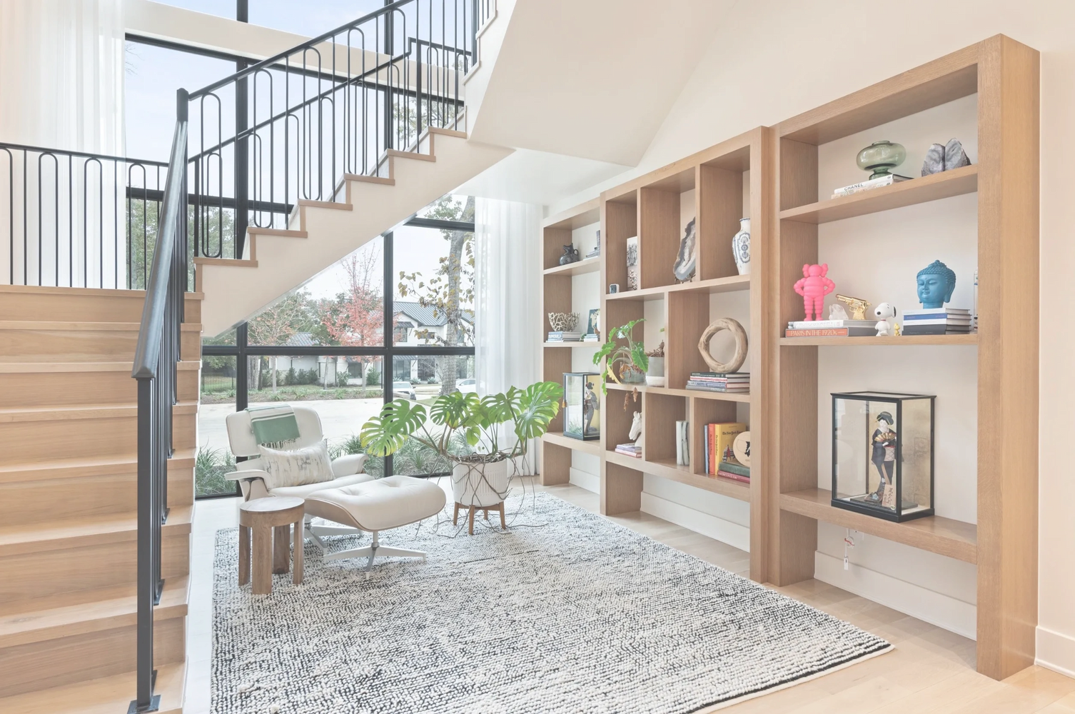 Modern cozy reading nook under a staircase with natural light and wooden shelves.