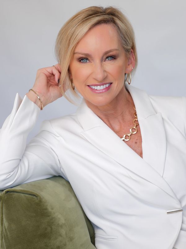 Smiling woman in white blazer posing on green sofa.
