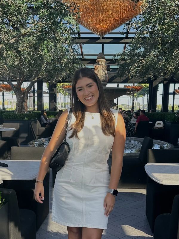 Smiling young woman in white dress at outdoor restaurant.