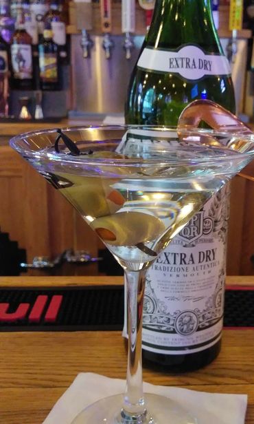 a dirty martini on a bar in front of a bottle of dry vermouth