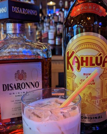 a white russian drink in front of a bottle of disaronno and a bottle of kahlua