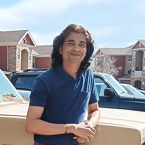 Man in a blue polo shirt smiling outdoors by parked cars.