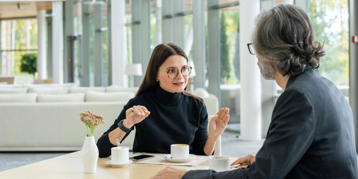 Two people having a calm, constructive conversation over coffee, exploring workplace differences.