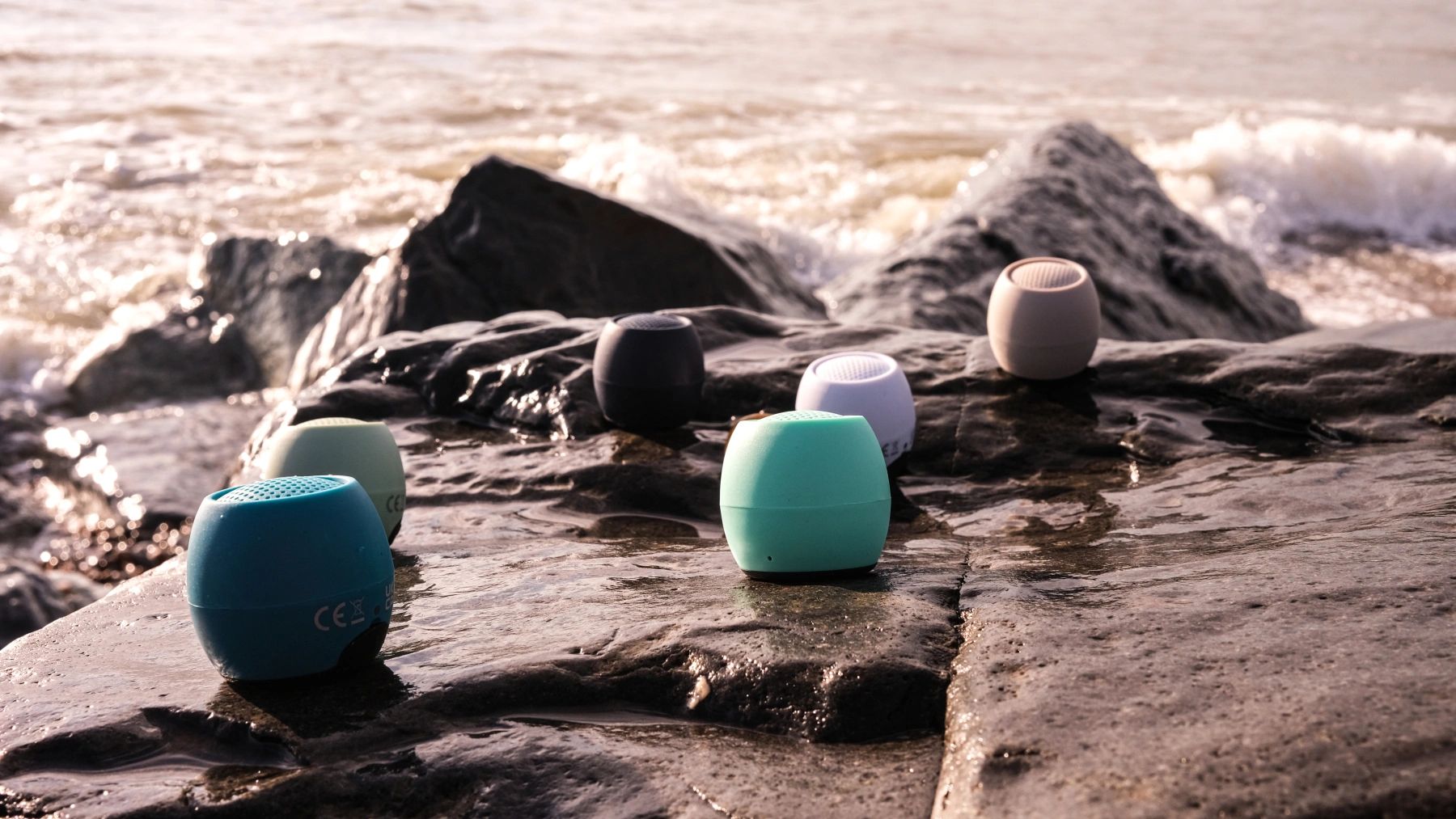 Colorful portable speakers placed on wet rocks by the sea shore.