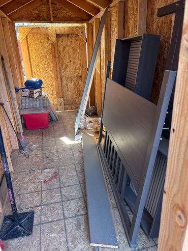 Inside of an unfinished wooden shed with construction materials and furniture parts.