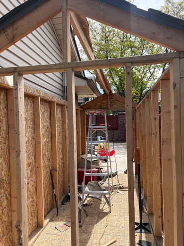 Wooden frame structure under construction beside a house.