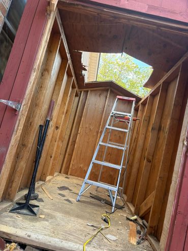 Wooden shed interior with a broken roof and ladder inside.