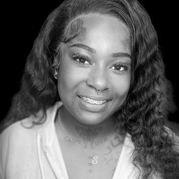 Smiling woman with tattoos, piercings, and curly hair wearing a white hoodie.
