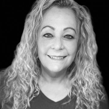Smiling woman with curly blonde hair in a blue shirt against a black background.