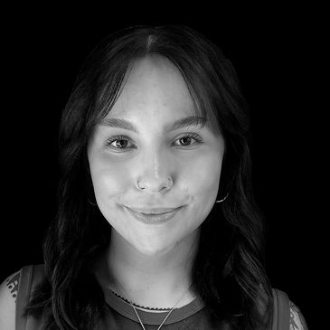 Smiling woman with tattoos wearing a Rolling Stones tank top against a black background.