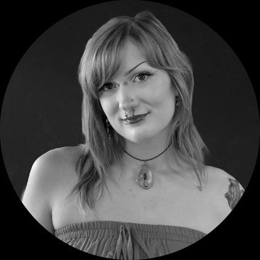 Woman with blue-green hair and facial piercings wearing an amber scorpion necklace.