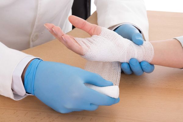 Doctor wearing blue gloves bandaging a patient's hand with gauze.