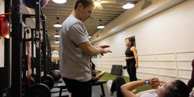 A man coaches a woman in a gym setting.