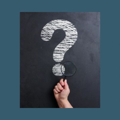 Hand holding magnifying glass over a chalk-drawn question mark on blackboard.