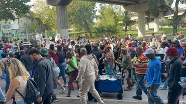 A diverse crowd enjoys a lively outdoor parade with a brass band under a bridge.