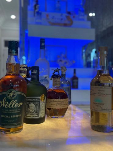 Various bottles of liquor on a glowing bar counter with blue-lit shelves in the background.