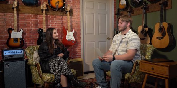 Two people sitting and talking in a music-themed room.