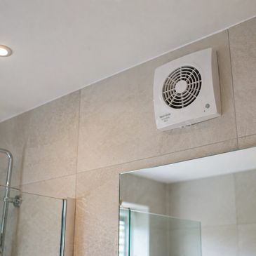 Bathroom ventilation fan installed on tiled wall above mirror.