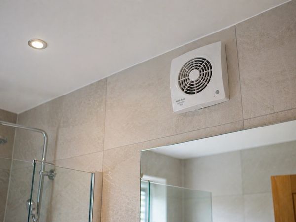 Bathroom exhaust fan installed on a tiled wall above a mirror.