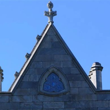 Gothic triangular stone rooftop with stained glass window and cross.