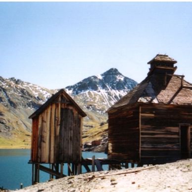 Rustic wooden cabins by a mountain lake under a clear blue sky.
