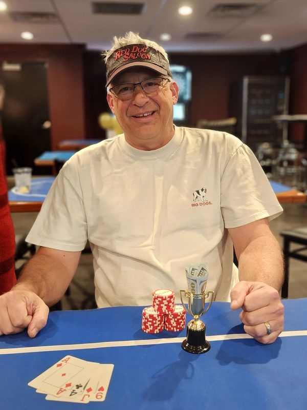 Man smiling with poker winnings and a small trophy.
