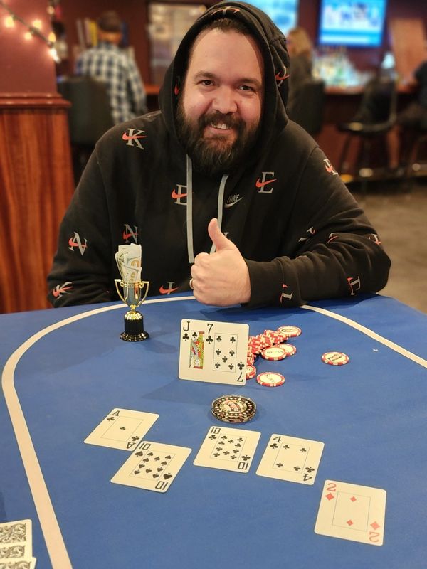 Man giving thumbs up at poker table with trophy and chips.