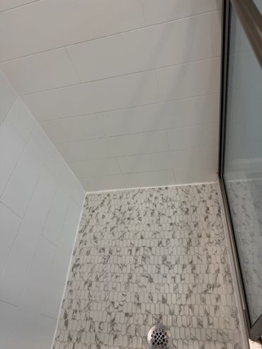 White tiled shower floor and walls with a glass door.