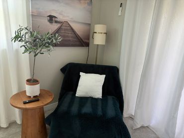 Cozy corner with a black chair, white pillow, plant, and serene pier artwork.