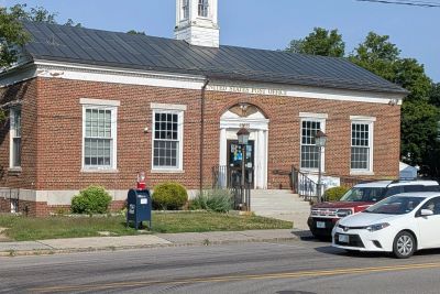 A brick post office building with cars and a mailbox in front.