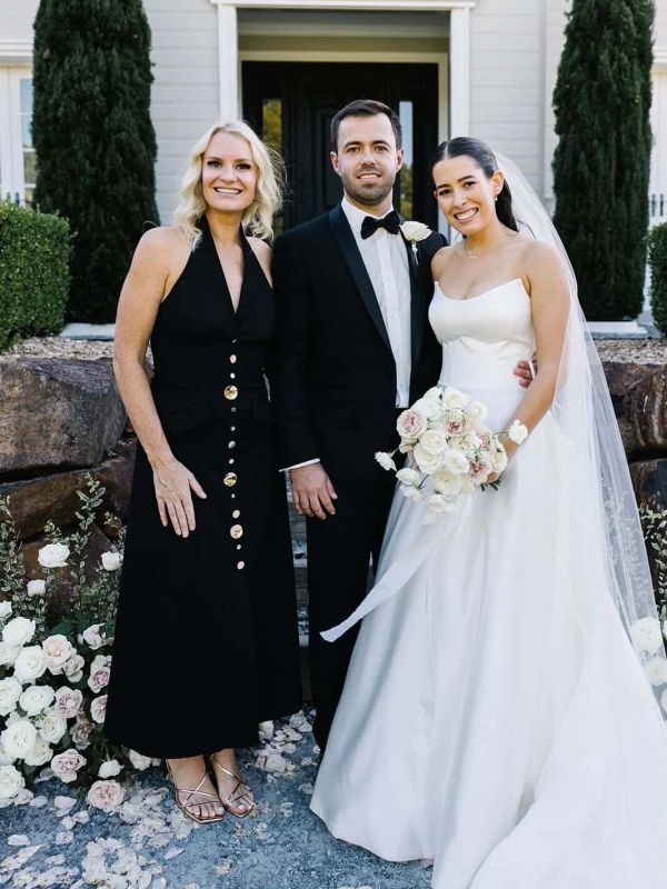 Bride, groom, and a guest posing happily outside a wedding venue.