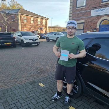 Young man proudly holding a practical driving test pass certificate in a parking lot.