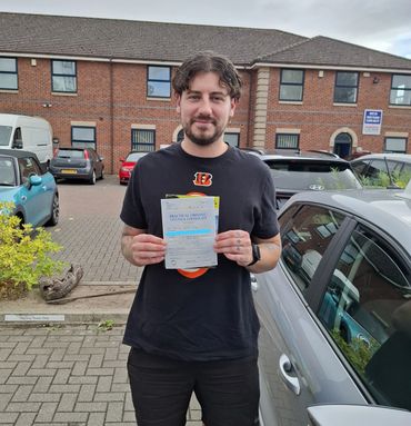 Man proudly holding a practical driving test pass certificate in a parking lot.