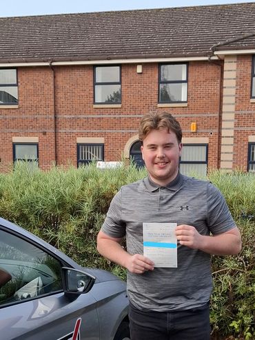 Young man proudly holding a practical driving test pass certificate beside a car.