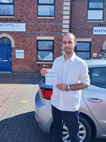 Man proudly holding a practical driving test pass certificate beside a car.