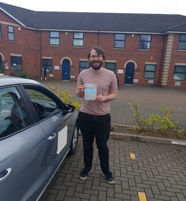Man proudly holding a practical driving test pass certificate beside a car.