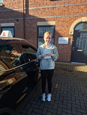 Young woman proudly holding her driving test pass certificate next to a learner driver car.