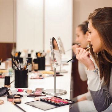Woman applying makeup in front of a mirror with makeup tools around.
