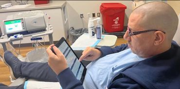 Man in medical setting using a tablet, connected to medical equipment.