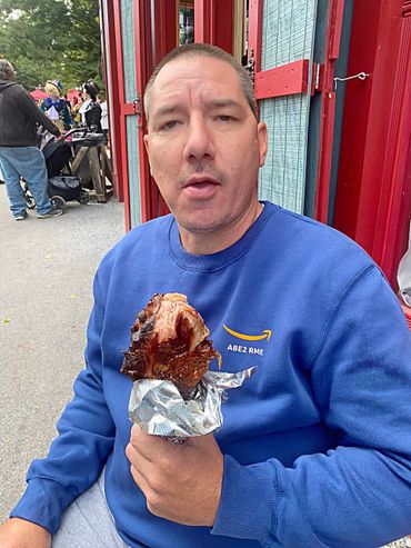Man in blue sweatshirt eating a large turkey leg outdoors.