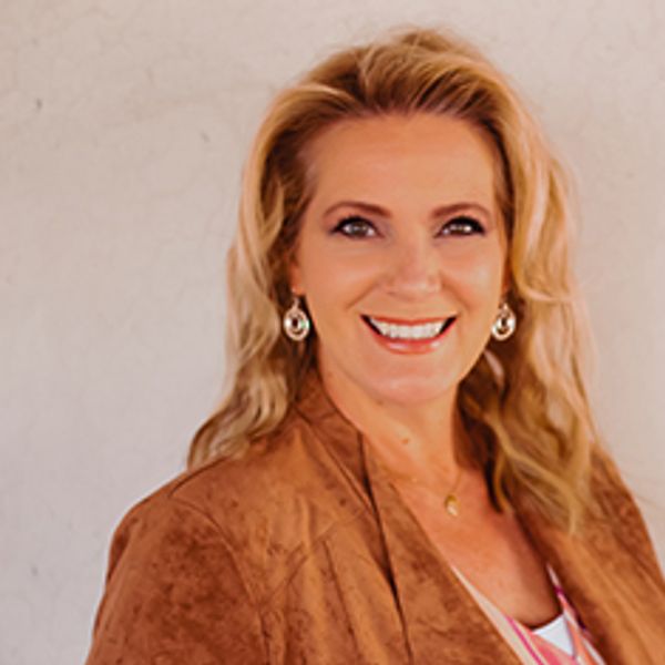Smiling woman with blonde hair wearing a brown jacket and earrings.