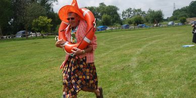 Man dressed festively with a witch hat and life ring, walking on grass.