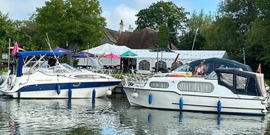 Boats docked near a riverside pub with trees and blue sky.