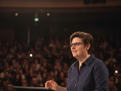Person speaking confidently at a podium to a large audience.