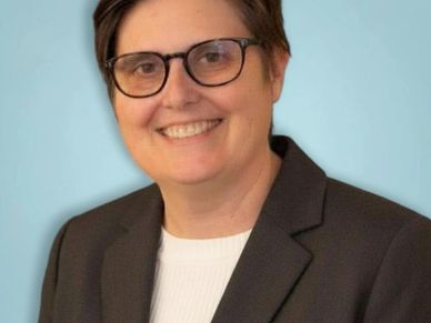 Professional portrait of a smiling person wearing glasses and a dark blazer.