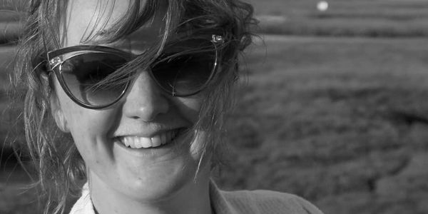 Close-up of a smiling woman wearing sunglasses with windblown hair.
