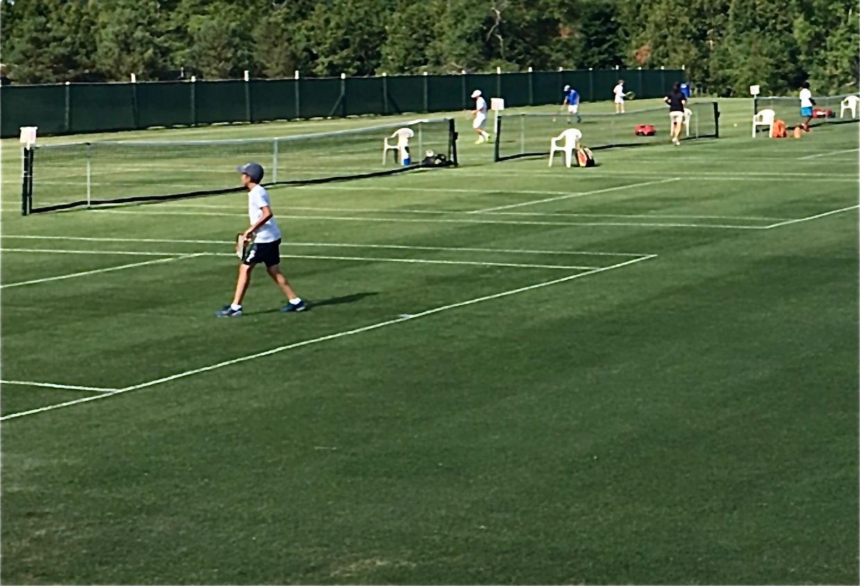 Young boys playing tennis on rows of grass tennis courts.